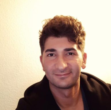 Junger Mann mit dunklem, lockigem Haar lächelt freundlich in die Kamera.